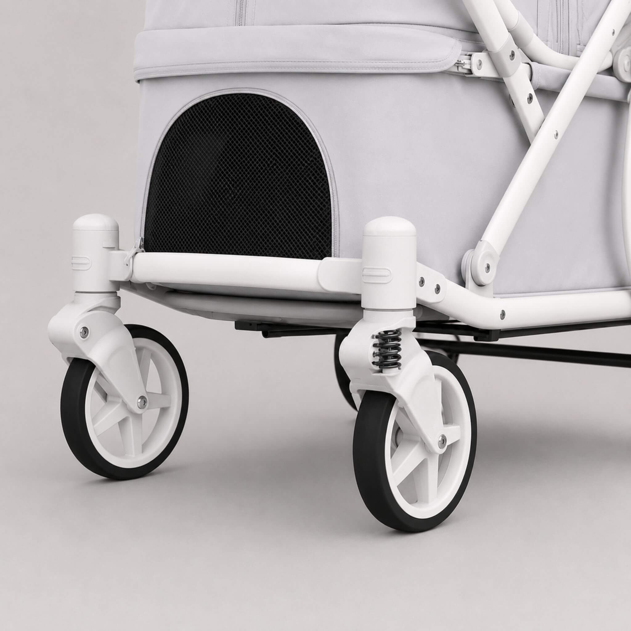 Close-up of the lower section of a stroller or pet stroller with a light gray fabric body, white frame, black mesh front panel, and black-and-white wheels on a clean light gray studio background.